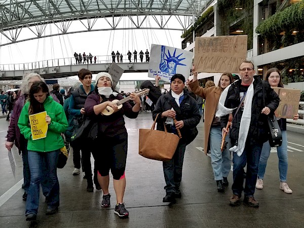 María Damaris plays her charango (left) while marching with Bajo Salario (including Leo Salazar, center with flute, and Paul Riek, right with the guitar-like jarana) at the Portland International Airport to protest the Muslim ban in January 2018: Photo by Douglas Yarrow